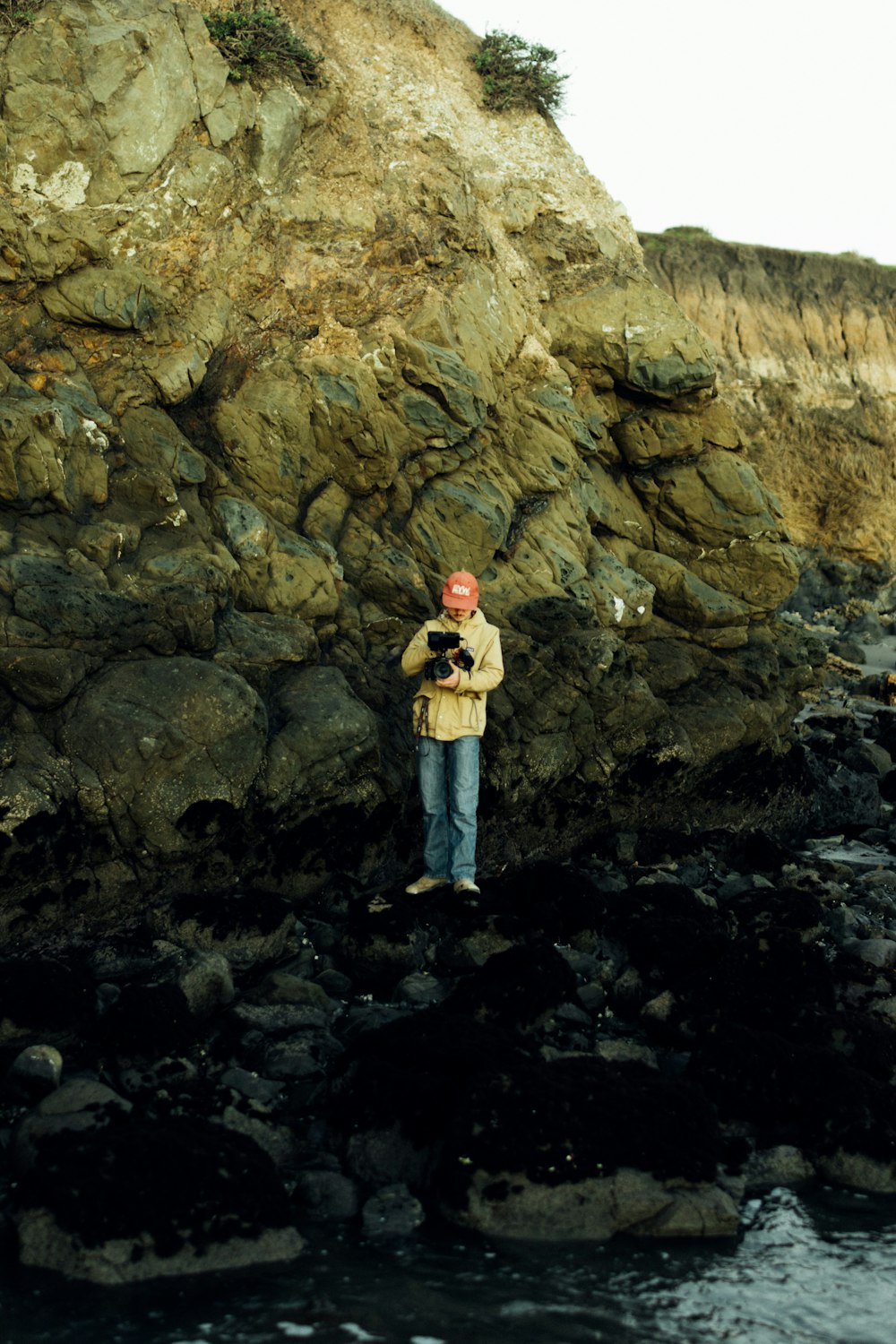 a man standing on a rocky beach next to a body of water