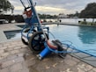 Close-up of a pool skimmer net and vacuum head resting beside a pool.