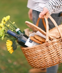 a person holding a wicker basket filled with food and wine
