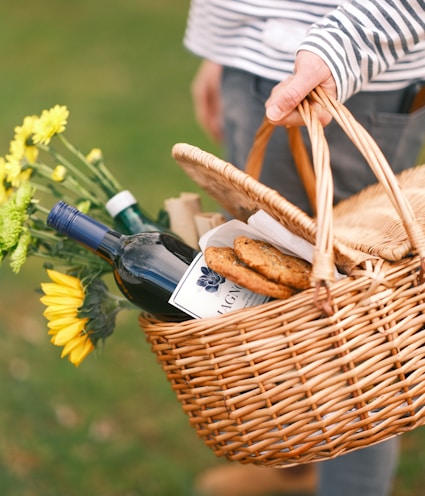 a person holding a wicker basket filled with food and wine