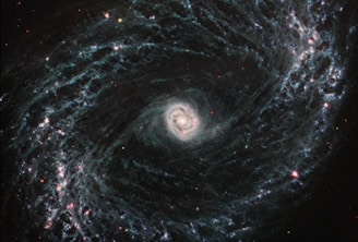 A stunning spiral galaxy with a bright central core surrounded by swirling arms of stars, dust, and gas. The arms are dotted with clusters of bright red and blue stars, creating a striking pattern against the dark backdrop of space.