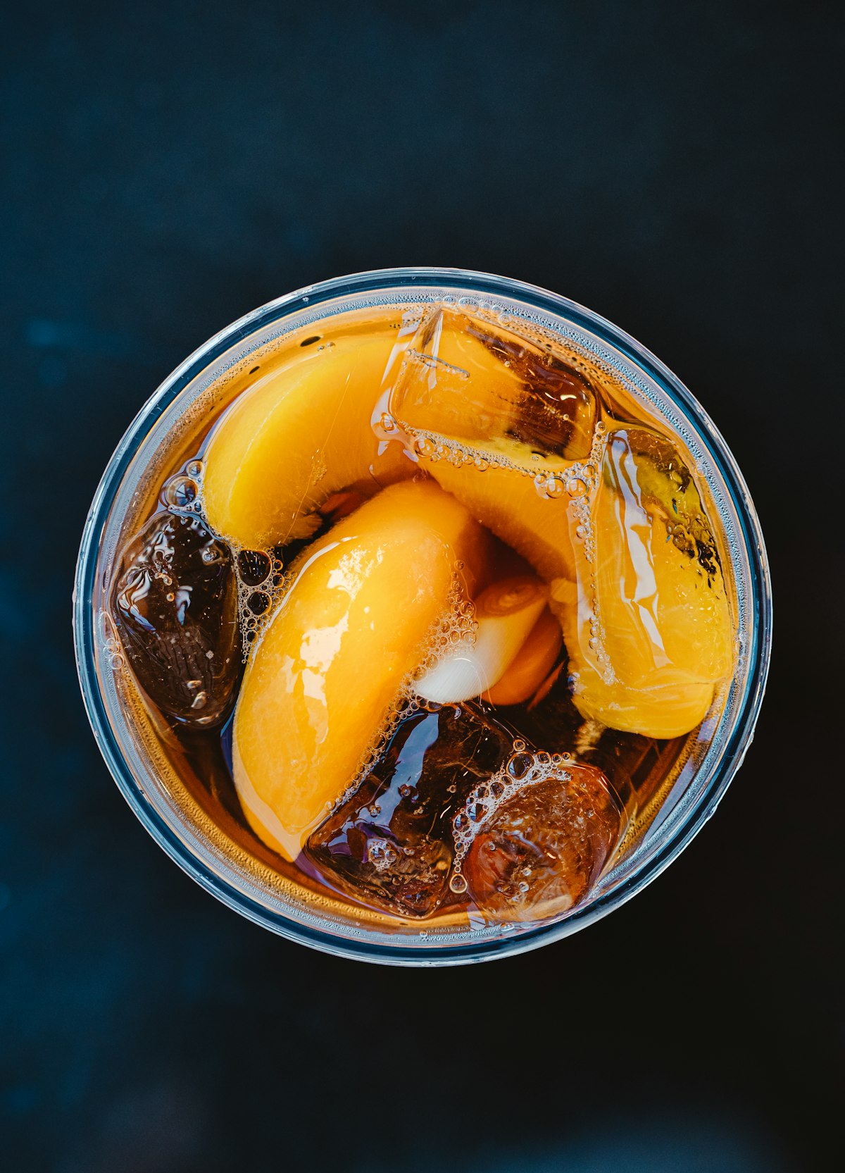 Overhead view of a glass of iced peach tea with fruit wedges and ice cubes