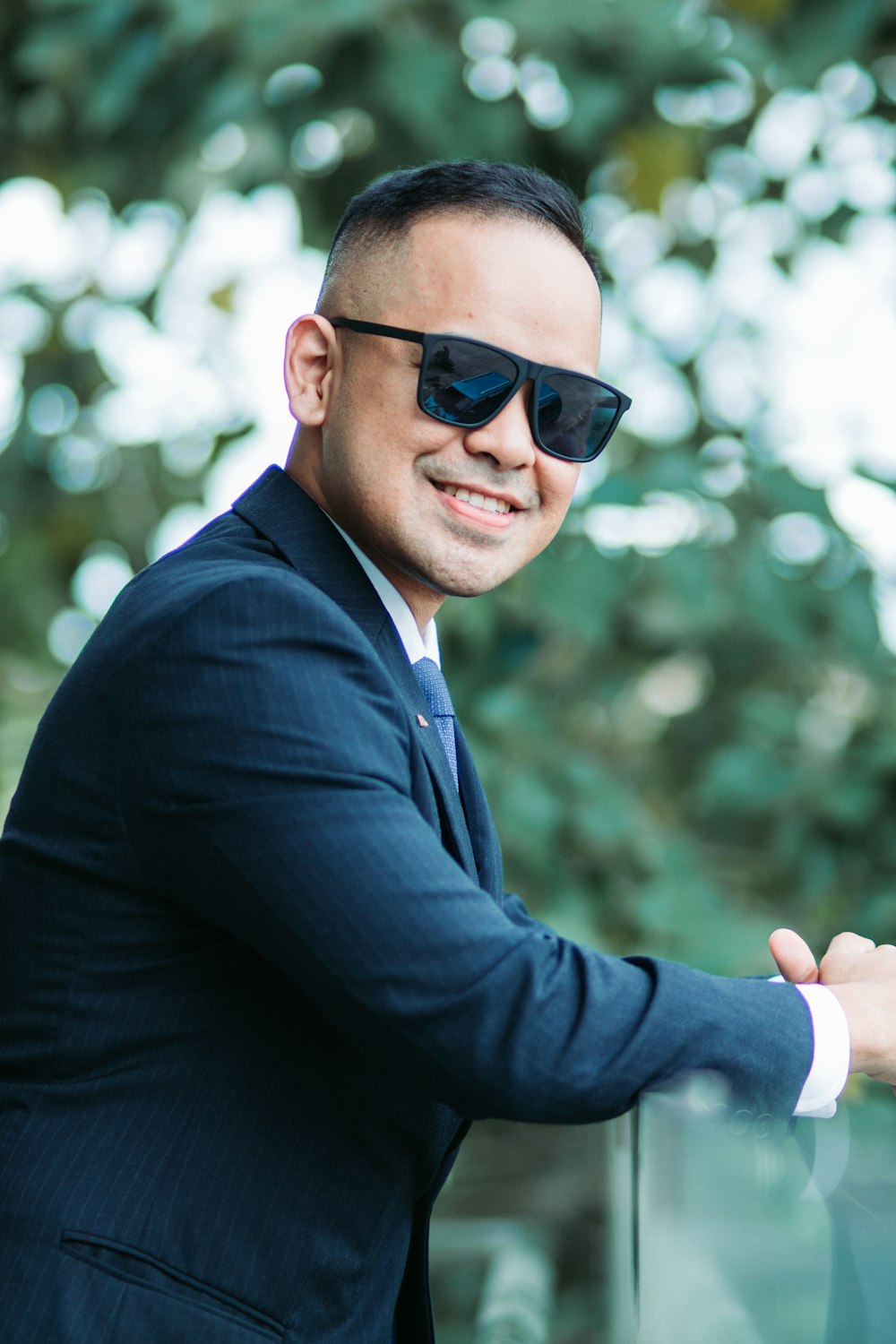 a man in a suit and sunglasses leaning against a fence