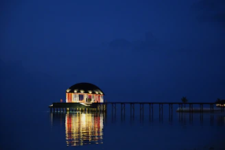 A shadowy overwater pavilion glowing softly against a gunmetal sea at night.