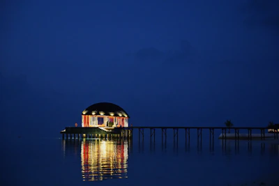 A shadowy overwater pavilion glowing softly against a gunmetal sea at night.
