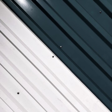 Metallic wall panels with parallel grooves. One side is a light cream color, and the other is dark green. Small bolts are visible, affixing the panels in place.