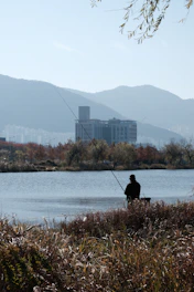 An angler casting a line into a calm river surrounded by autumn foliage.