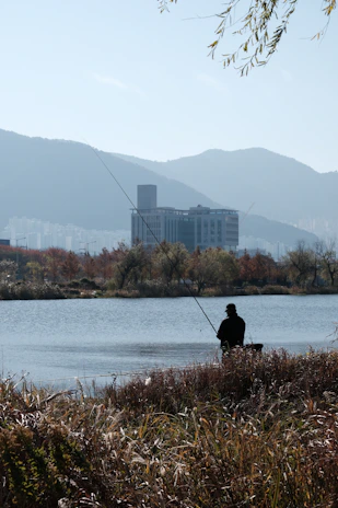 A fisherman casting a line into a calm river surrounded by autumn foliage.
