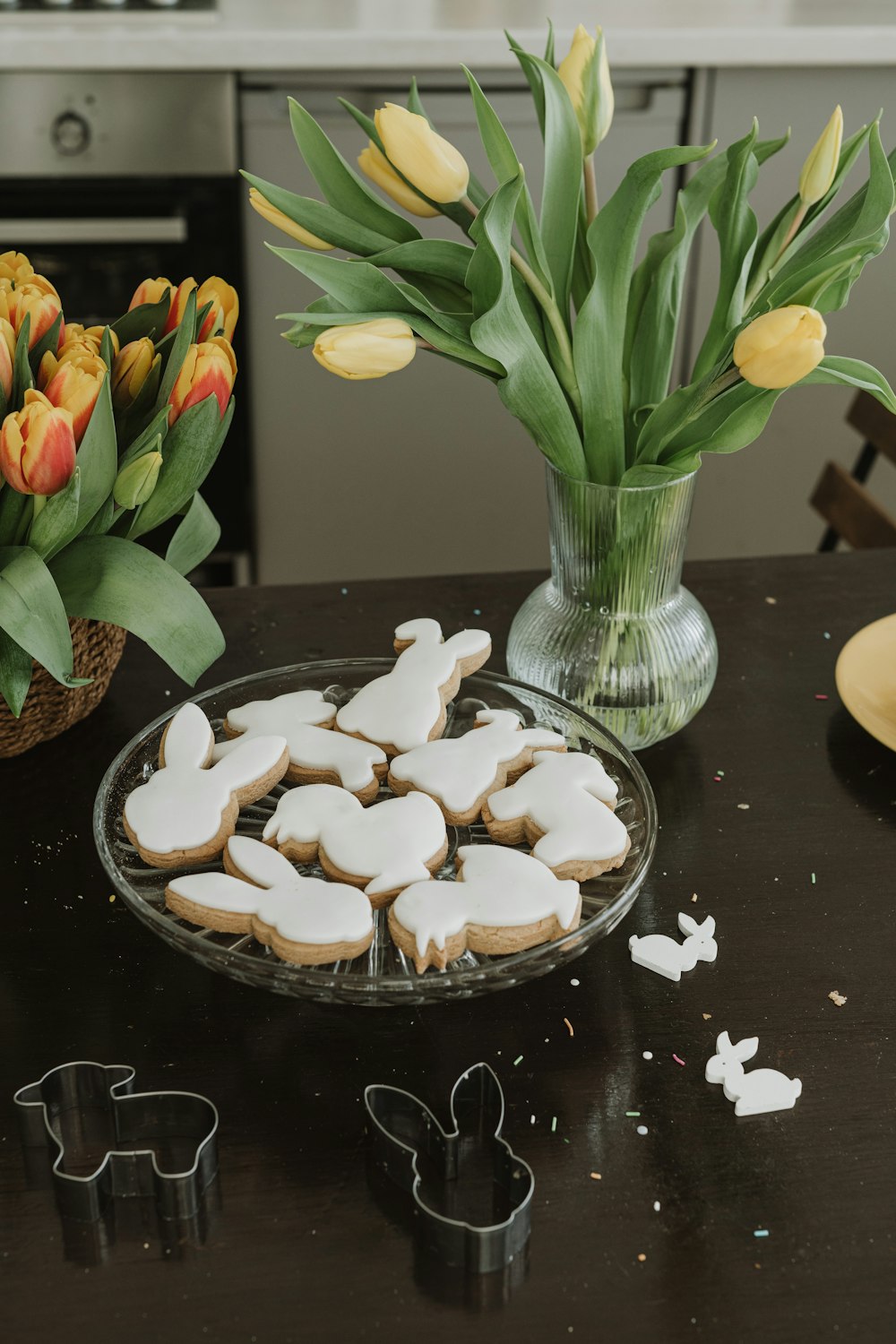 una mesa cubierta con un plato de galletas junto a un jarrón de tulipanes