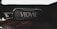 A rectangular, rugged Bluetooth speaker with the brand name 'VIDVIE' prominently displayed on the front sits on a wooden surface. The lighting is dim, casting shadows around the speaker, and a paper stapler is partially visible to the side.