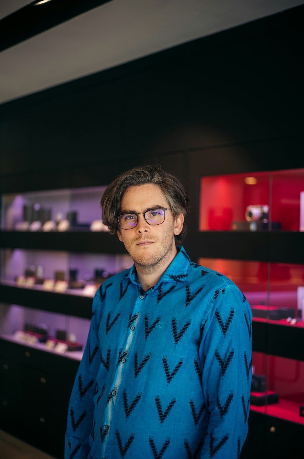 a man wearing glasses standing in front of a display case