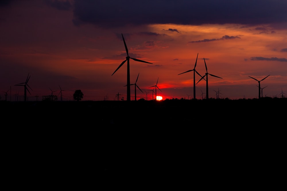 a group of windmills are silhouetted against a sunset