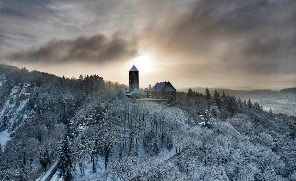 Tall tower and church stand on hilltop amidst snow-covered trees under bright sunlight