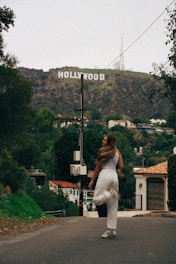 a woman walking down a street in front of a hollywood sign