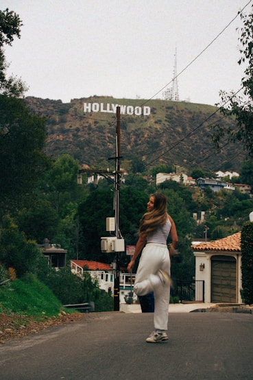 a woman walking down a street in front of a hollywood sign