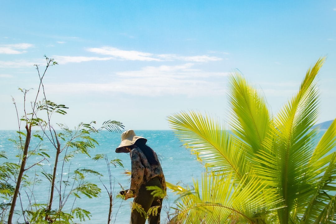 a man with a hat standing on a cliff overlooking the ocean