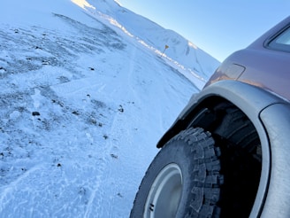 A close-up of a car tire on a rocky trail with snow-capped peaks in the background.