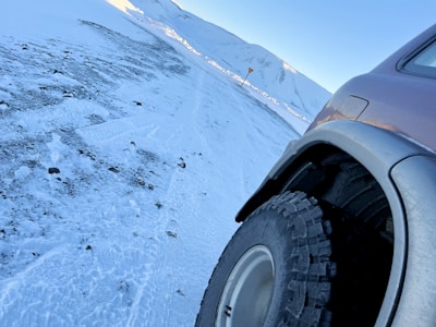 Close-up of snow tires on a 4x4 vehicle parked on a snowy alpine path.