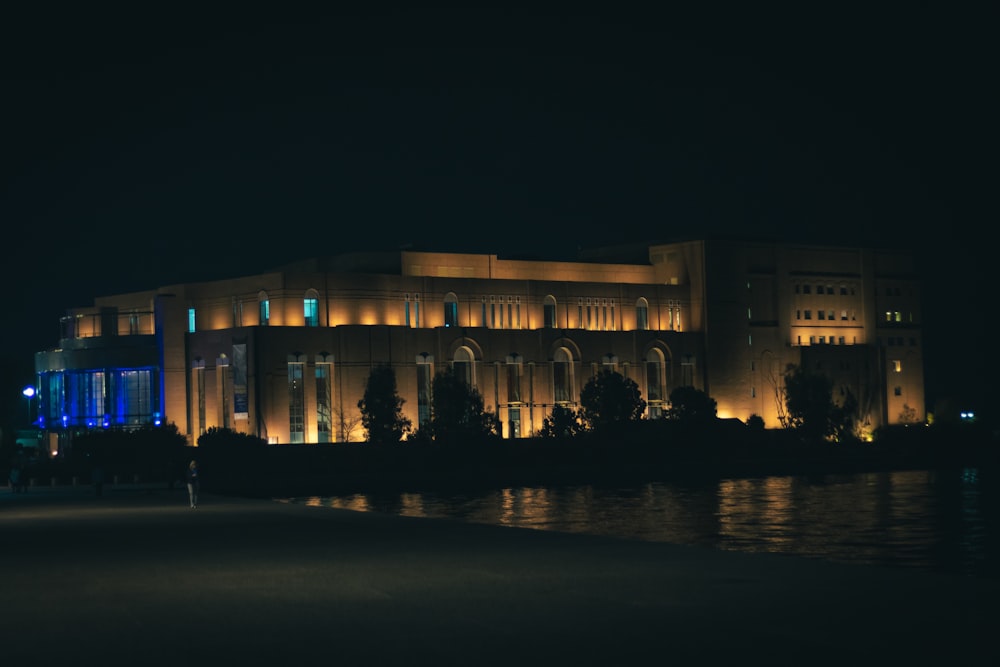 Un gran edificio iluminado por la noche con un cuerpo de agua frente a él