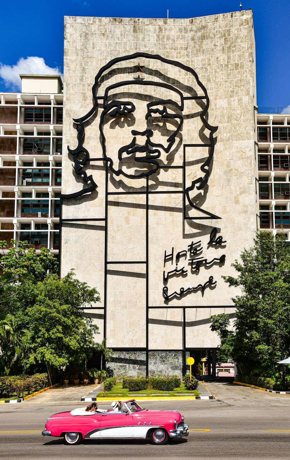 a pink car driving past a tall building with a giant painting on it's