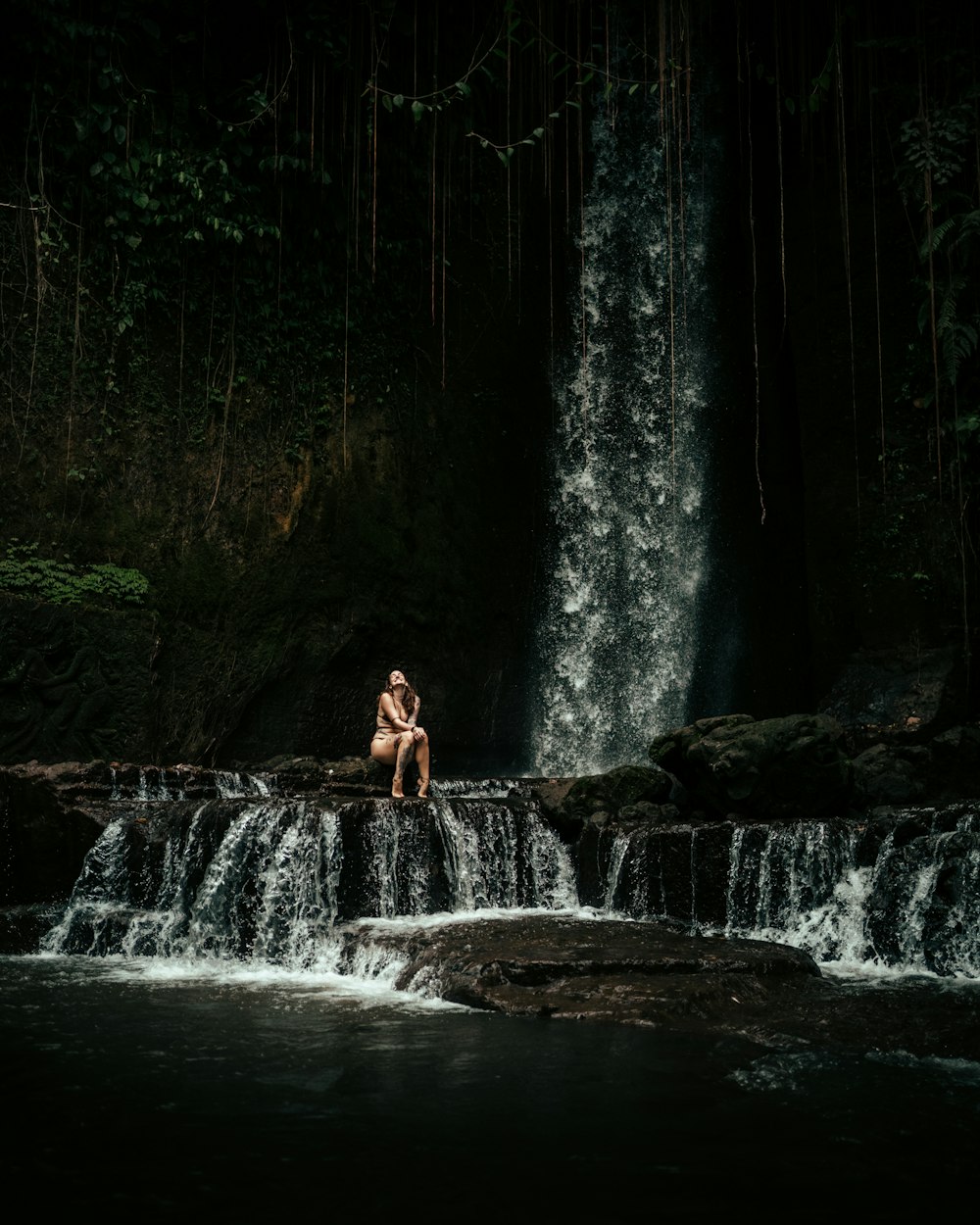 a person sitting on a rock in front of a waterfall