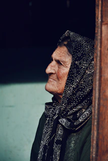 An elderly woman gazing thoughtfully at ancient ruins, a gentle breeze playing with her scarf.