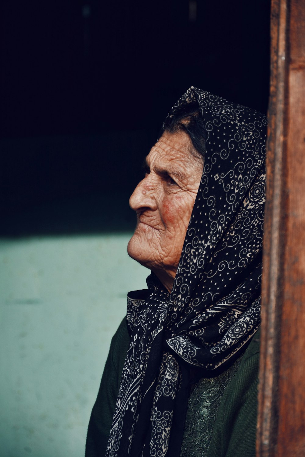 an old woman wearing a headscarf looking out a window