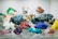 A variety of colorful mineral samples displayed on a reflective surface. The minerals are of different shapes, sizes, and colors, including striking reds, blues, greens, yellows, and purples.