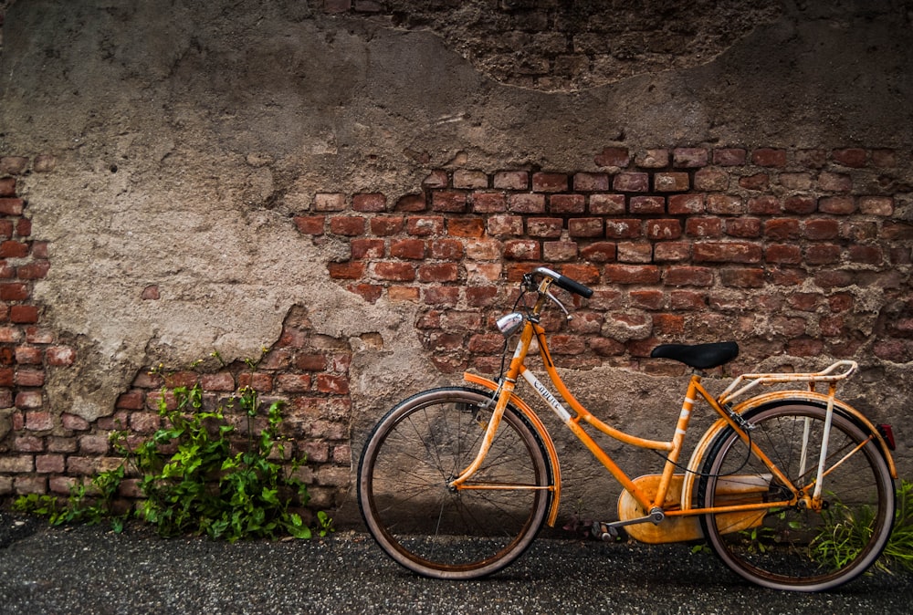 an orange bike parked next to a brick wall