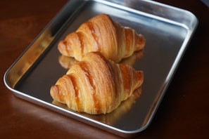 A tray of golden croissants fresh out of the oven, resting on a black baking sheet