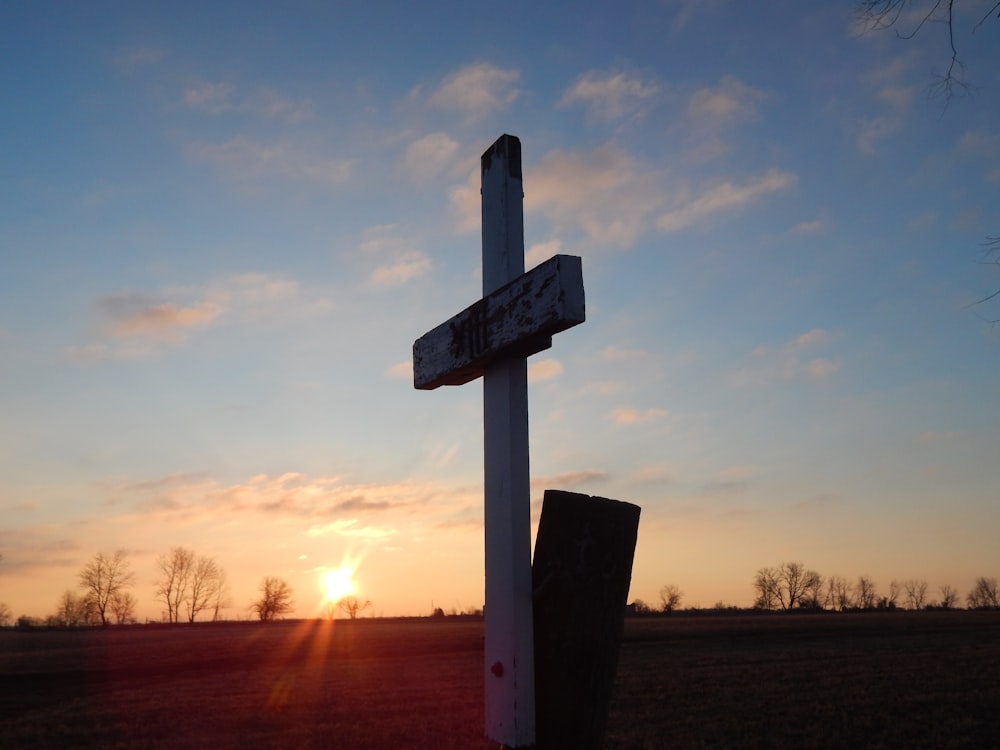Una cruz en un campo con la puesta de sol en el fondo