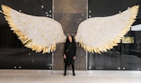A woman standing in front of a large angel wings sculpture