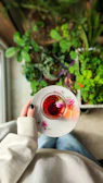 A cozy corner with a woman sipping herbal tea, surrounded by plants and soft natural light.