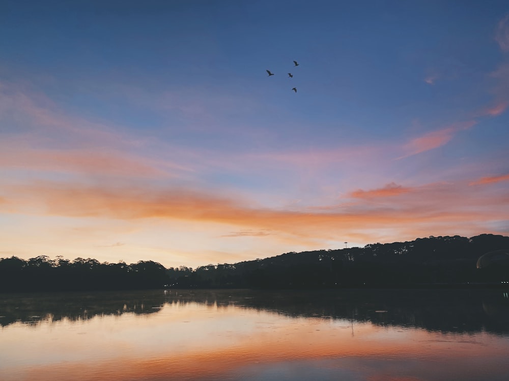 a sunset over a lake with birds flying in the sky