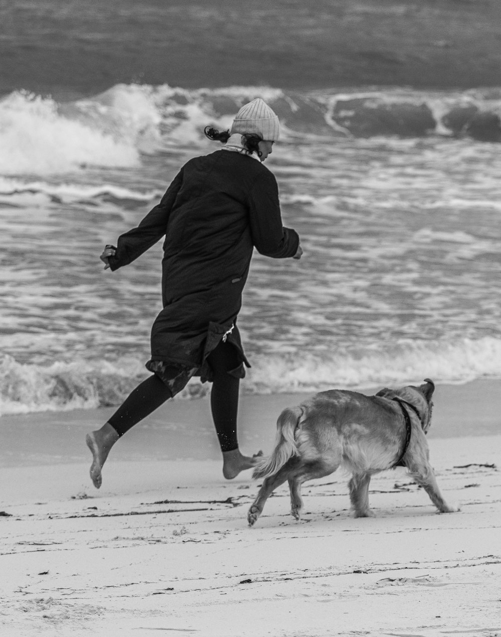 a person running on a beach with a dog
