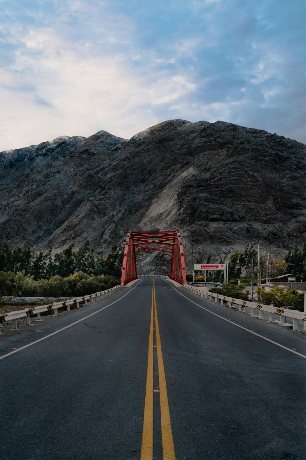 a road with a red bridge and mountains in the background