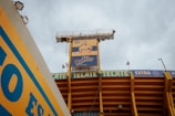 A stadium structure with a large advertisement for Ruffles featuring a person wearing a yellow shirt is prominently displayed. The stadium is painted in yellow and blue, with the brand names 'Tecate' and 'Extra' visible along the upper sections of the structure.