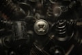 A close-up view of various black metal screws and fasteners, with one silver screw prominently in focus. The background is blurred, creating a dark, industrial atmosphere.