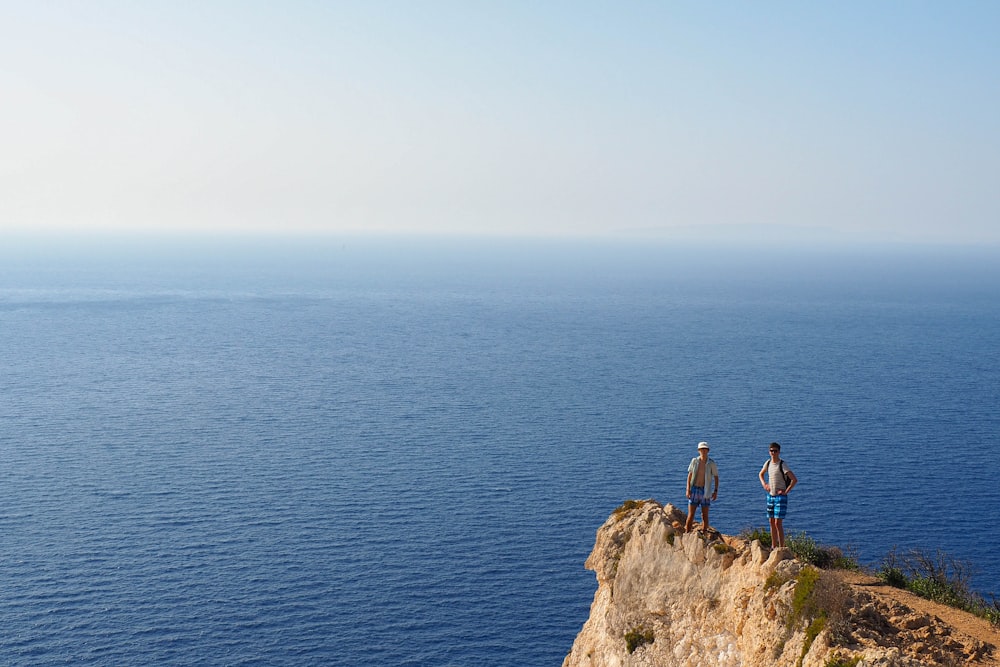 two people standing on a cliff overlooking the ocean