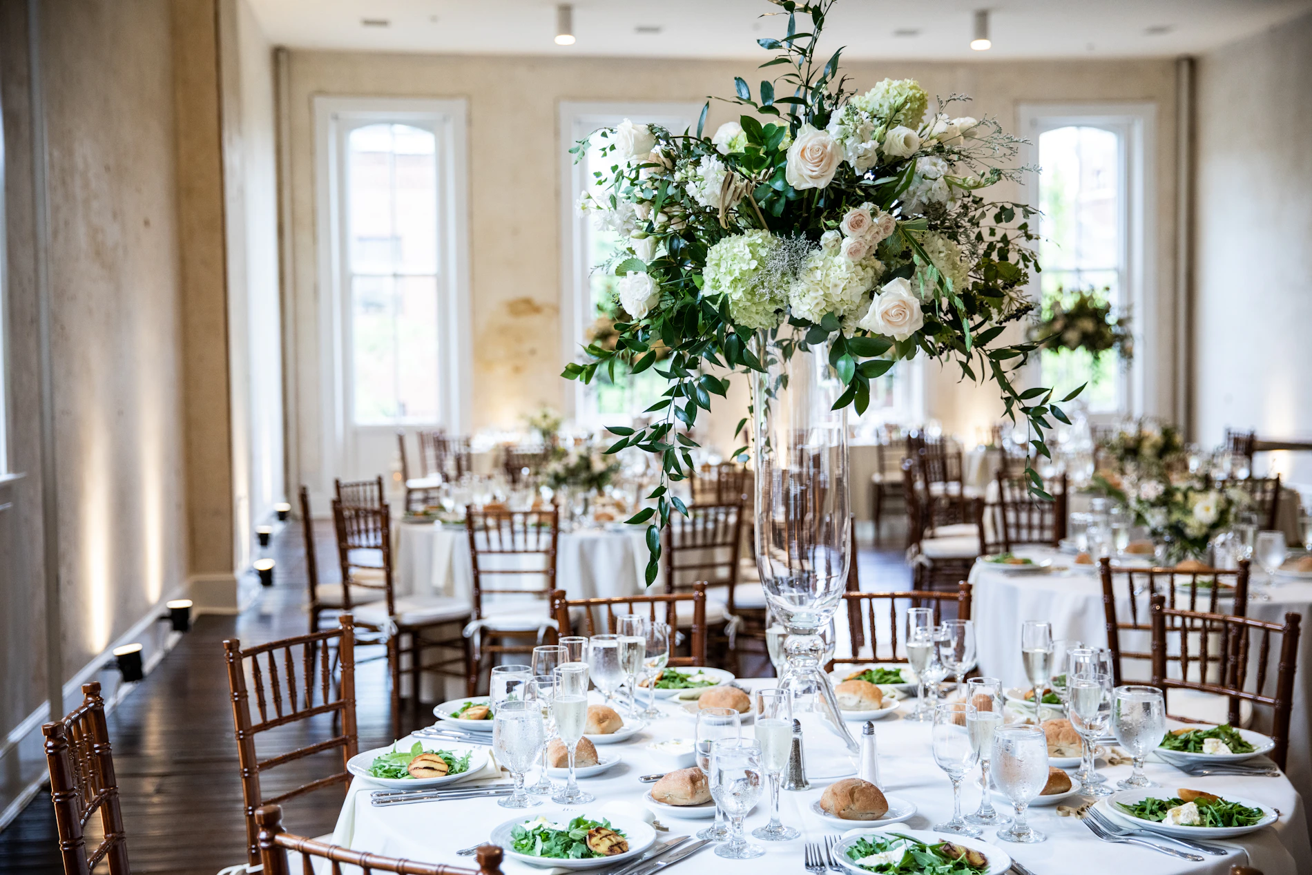Formal celebration table with white flowers, greenery, plates, glassware, and elegant place settings