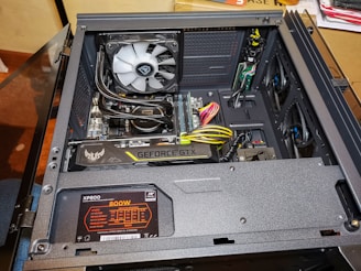 An open computer case reveals various internal components including a graphics card labeled 'Geforce GTX', a power supply unit marked 'XP800 800W', and a cooling fan. There are several visible cables and wires, some of which are neatly organized. The build appears clean and professionally assembled.