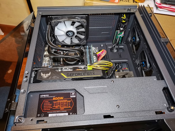 An open computer case reveals various internal components including a graphics card labeled 'Geforce GTX', a power supply unit marked 'XP800 800W', and a cooling fan. There are several visible cables and wires, some of which are neatly organized. The build appears clean and professionally assembled.