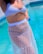 A person is standing beside a pool, wearing a striped bikini top and a sheer, polka dot skirt or cover-up. The water in the pool is a bright blue, giving a refreshing look.