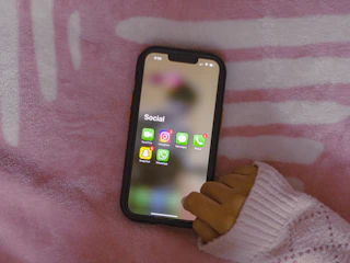 Hands holding a smartphone showing colorful social media icons with a soft pink and gold background.