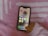 A smartphone displaying a social media folder is being held by a hand wearing a pink sweater. The background consists of a pink and white patterned fabric.