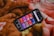 A smartphone displaying a music or podcast app screen is placed on a warm, fuzzy blanket. The phone screen shows various categories like 'Telugu,' 'Punjabi,' 'Podcasts,' and others, each highlighted in different colors. The blanket has a soft texture with shades of brown, orange, and red.