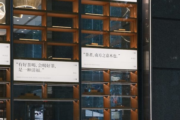 A modern, visually appealing wall display featuring quotes in both Chinese and English. The wall consists of multiple rectangular sections with mirror-like surfaces and ambient lighting. Wood accents highlight the design, creating a sophisticated and warm atmosphere. Some sections reflect elements from the surrounding environment, enhancing the overall aesthetic.