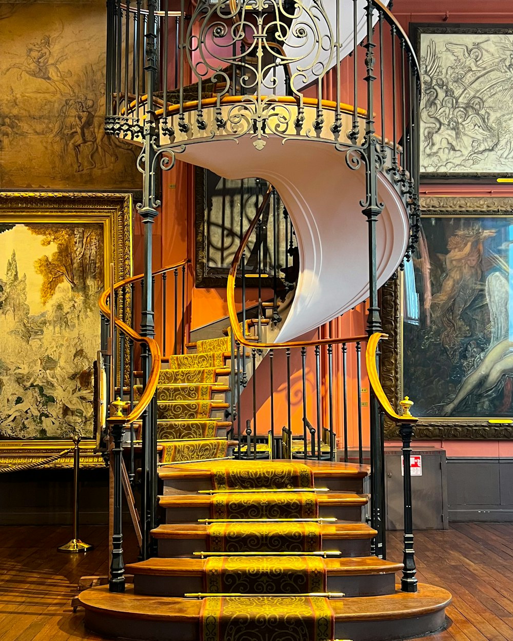 a spiral staircase in a museum with paintings on the walls