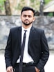 a man in a suit and tie standing in front of a stone wall