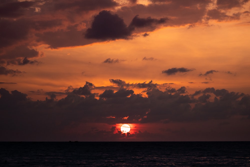 the sun is setting over the ocean on a cloudy day